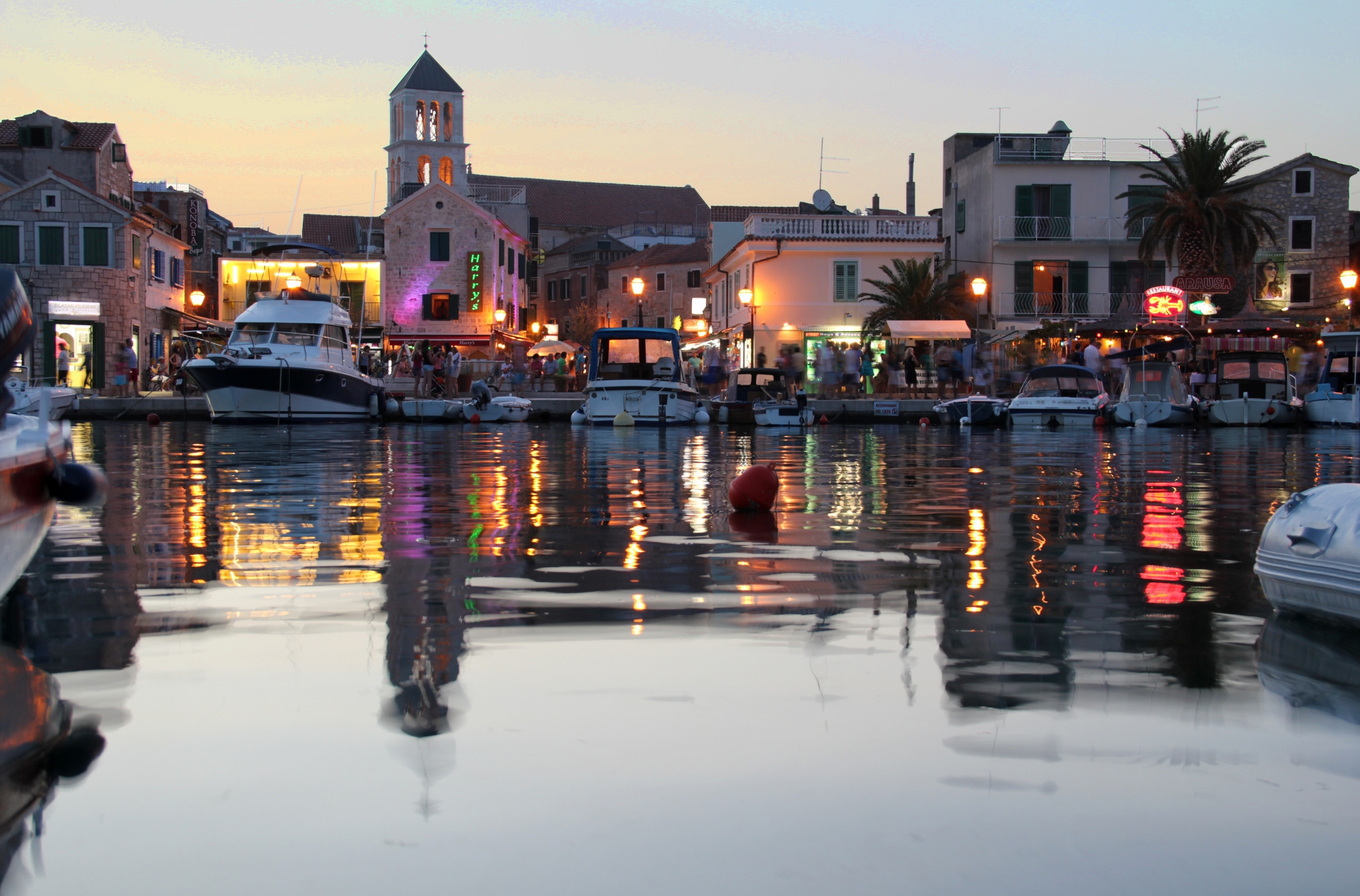 De haven van Vodice bij avond, met boten, verlichte terrassen en de kerktoren